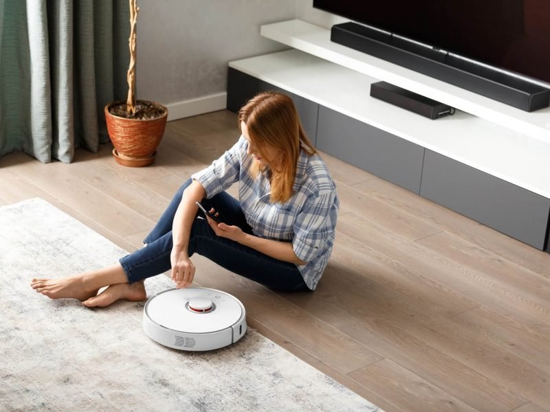 the-girl-sits-on-the-floor-and-controls-the-robot-vacuum-cleaner-using-a-smartphone-smart-home-.jpg